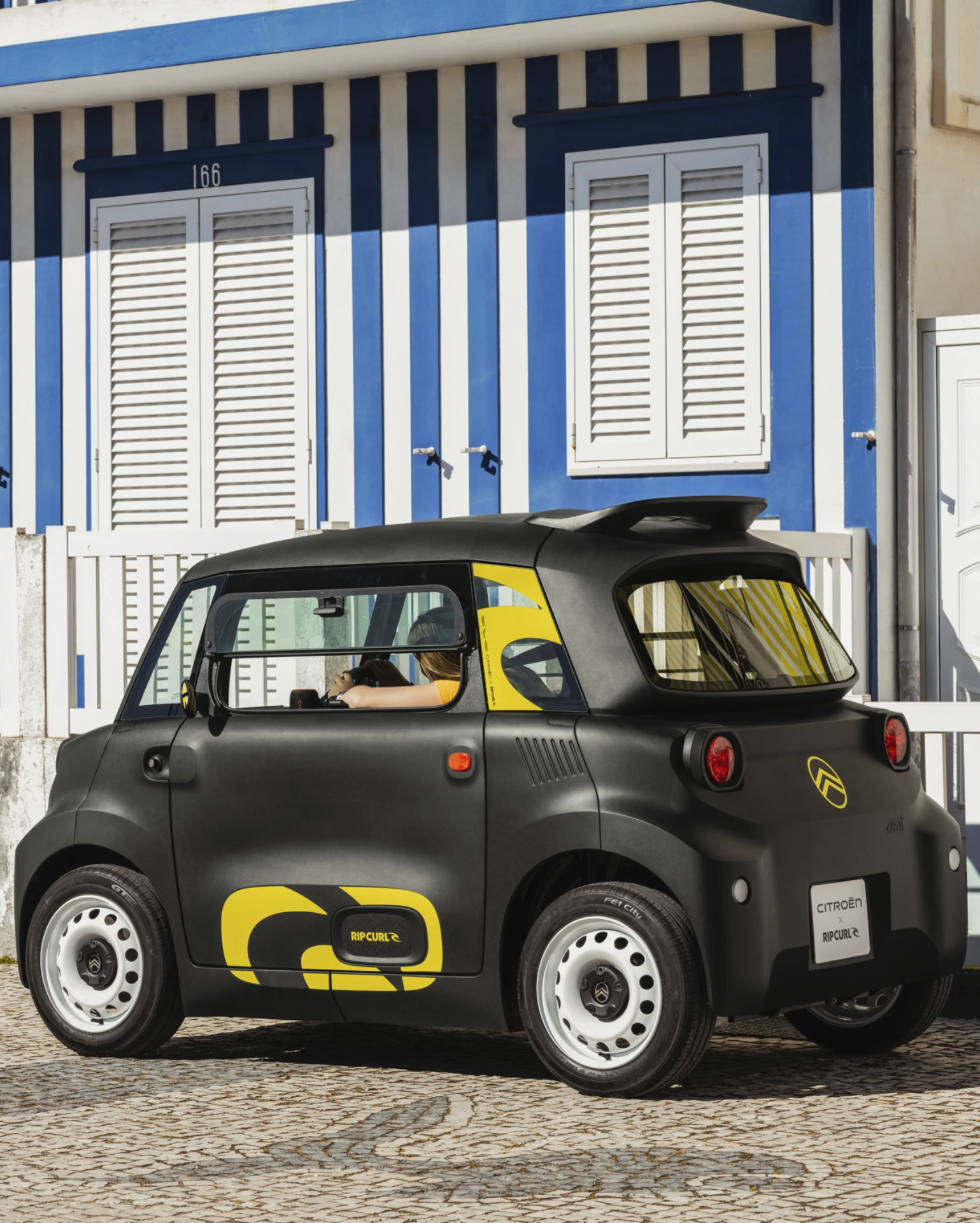 Vue arrière latérale de la Citroën Ami x Rip Curl électrique sans permis, Citroën Ami : plus sûre avec ses quatre roues pour une voiture électrique urbaine